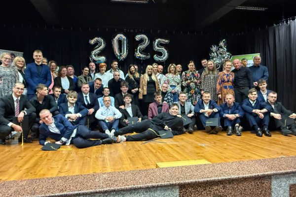 Duża grupa ludzi, w tym dorośli i nastolatkowie w formalnych strojach, pozuje razem na scenie z dekoracjami z balonów 2025 w tle. Niektórzy ludzie stoją, podczas gdy inni siedzą lub leżą na podłodze.